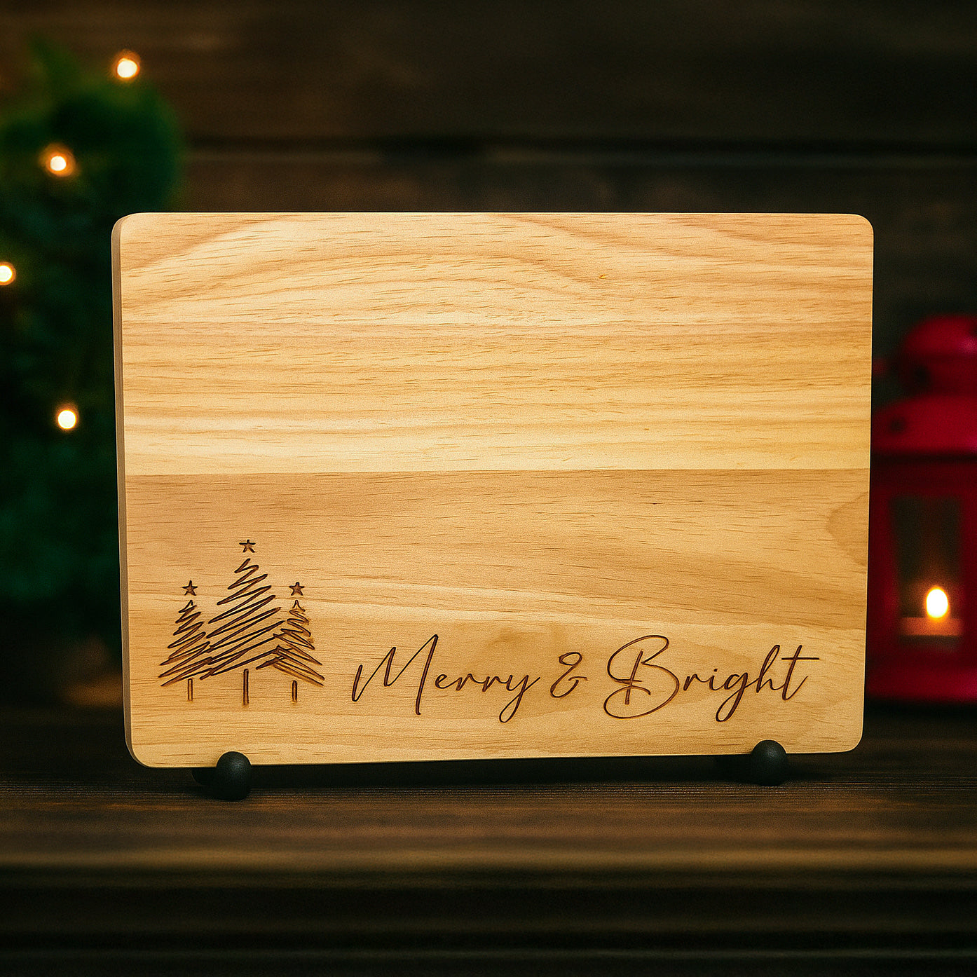 Wooden cutting board with Christmas tree design and 'Merry & Bright' text, placed on a wooden surface with festive decorations.